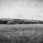 Black and white photo of a field with a row of identical townhouses in the background