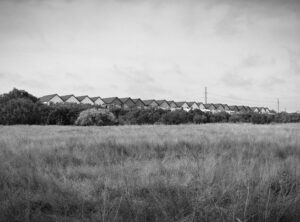 Black and white photo of a field with a row of identical townhouses in the background